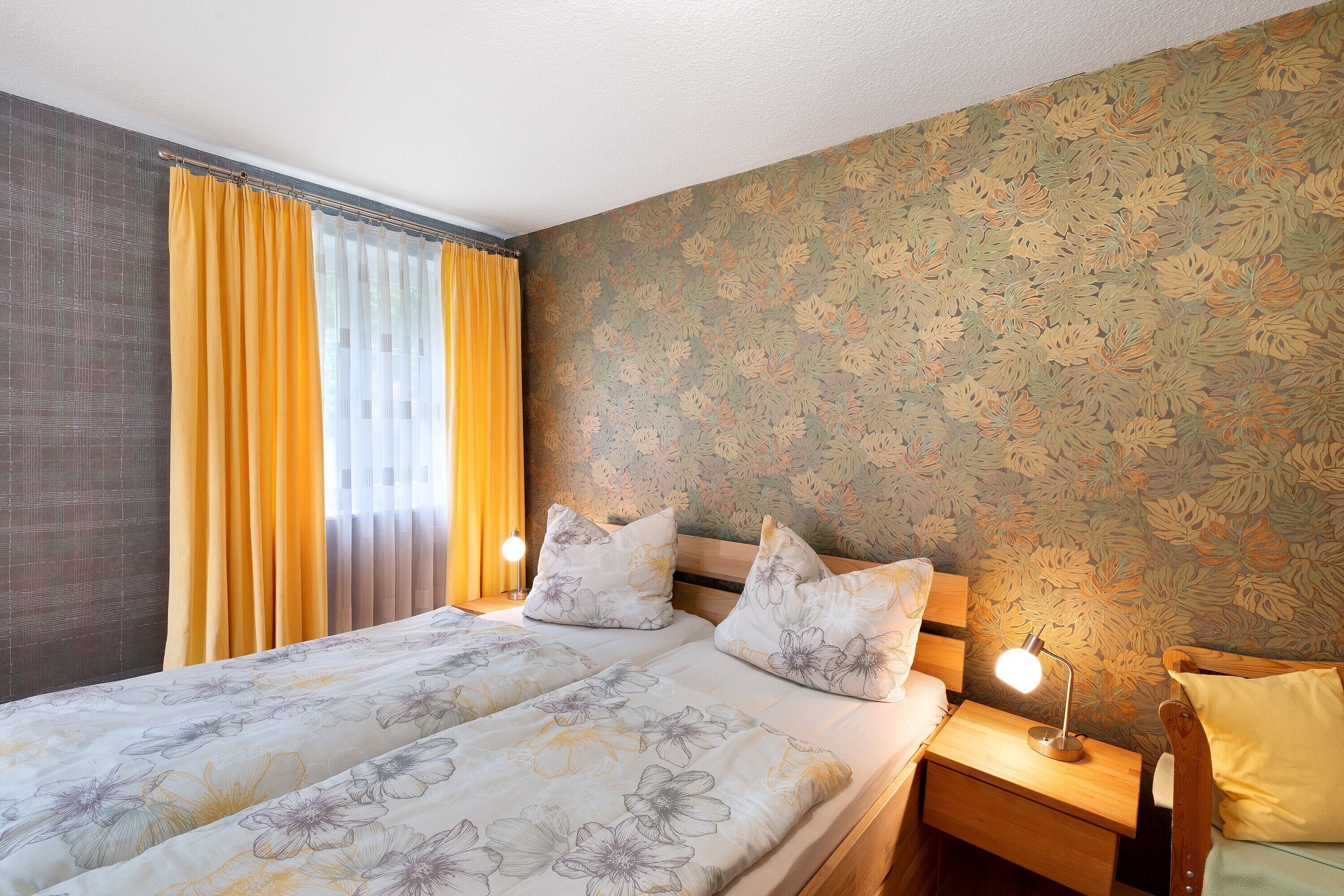 A bedroom with a bed, two bedside tables, a night lamp, and a window with curtains.