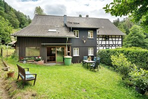 A house with a dark exterior, a tiled roof, and a front porch with a bench and table.