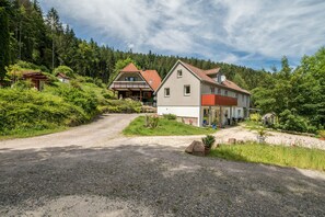 A residential area with houses, a gravel driveway, and a forested backdrop.