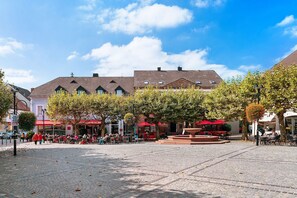 Una plaza empedrada con mesas al aire libre, árboles y edificios al fondo.