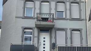 A two-story building with a grey facade, a white door, and a balcony with a metal railing.