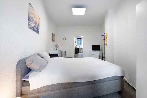 A bedroom with a bed, a desk, a chair, a radiator, and a television.