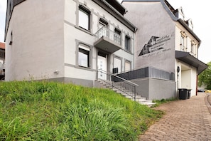 A building with a balcony, a staircase, and a trash bin.