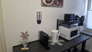 A kitchenette with a coffee maker, microwave, and a coffee cup on the counter.