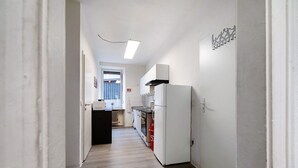 A narrow hallway with a kitchen area, including a refrigerator, oven, and cabinets.