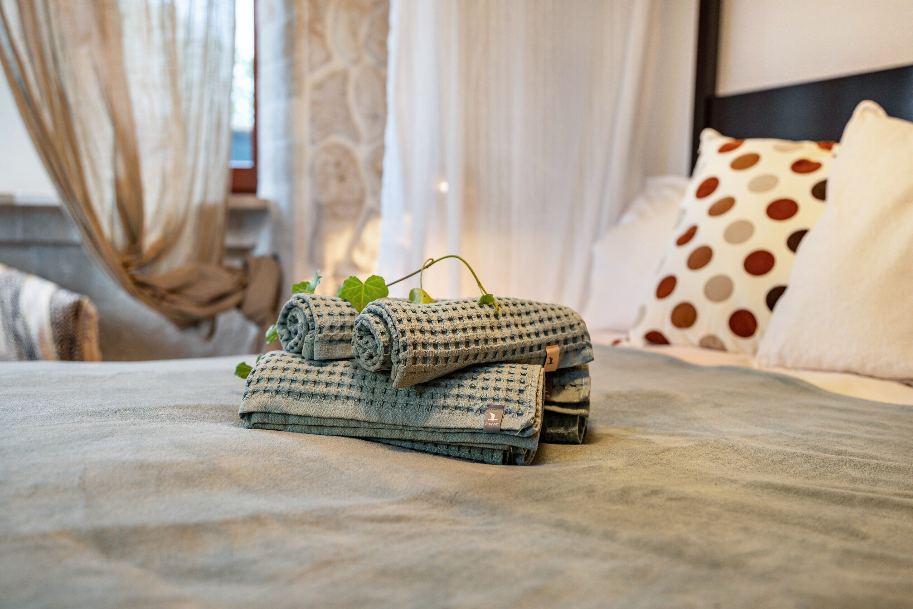 A neatly made bed with rolled towels and a polka dot pillow.