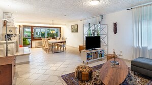 A modern living room with a flat-screen TV, a dining area with chairs, a sofa, and a coffee table. - Apartment 'Schwarzwald Glück Ferienwohnung' with Private Terrace and Wi-Fi (Bühl)