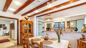 A dining area with wooden chairs, a table with placemats, a hanging light fixture, and a view into the kitchen. - Apartment 'Schwarzwald Glück Ferienwohnung' with Private Terrace and Wi-Fi (Bühl)