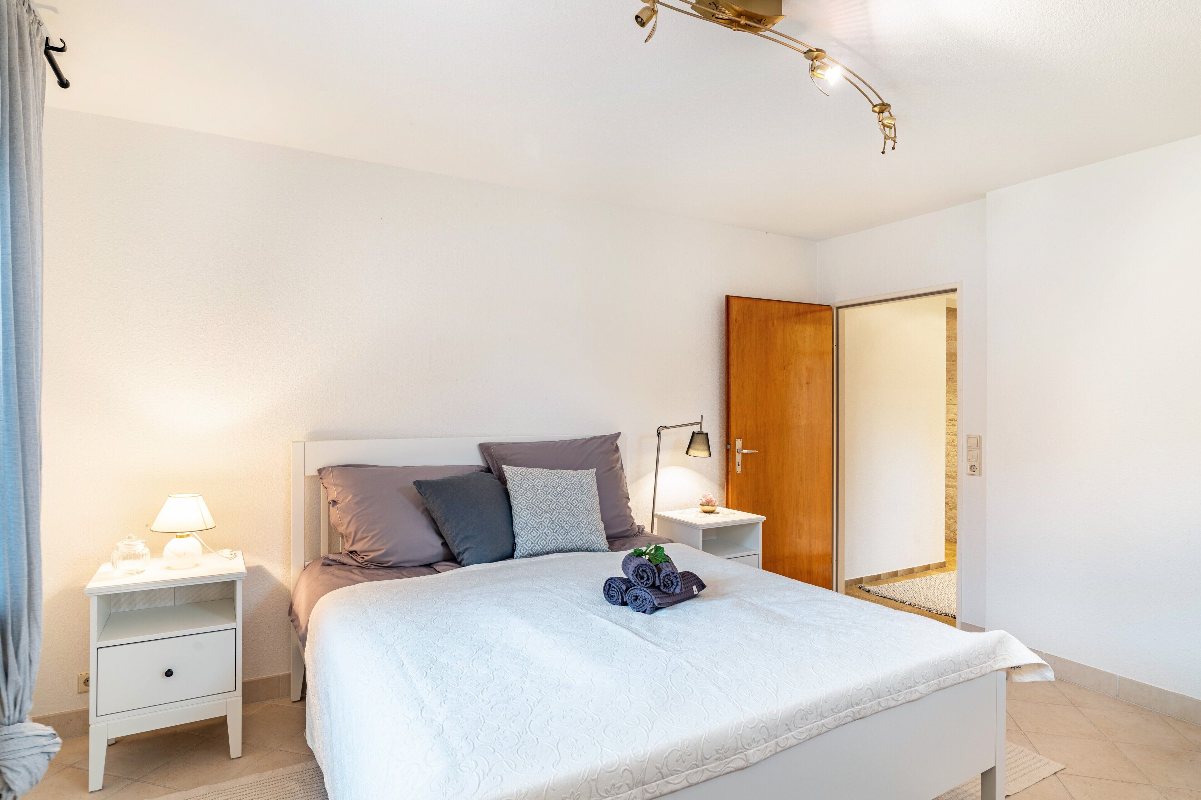 A neatly made bed with a white comforter, a bedside lamp, and a nightstand with a lamp.