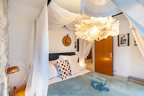Une chambre à coucher avec un lit, des rideaux blancs, une porte en bois, une horloge murale et un tableau.