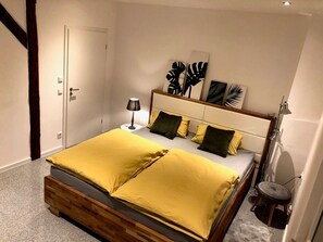 A bed with a wooden frame, a bedside table, a lamp, and artwork on the wall. - Dream Loft Winter Garden Apartment with Shared Terrace, Wi-Fi & Air Conditioning (Schwabach)