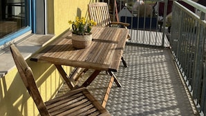 Un balcon avec une table et des chaises, un pot de fleurs et une vue sur un lac et une forêt.