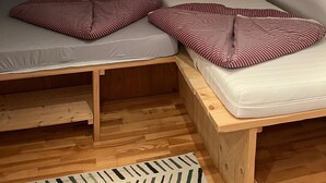 Une petite chambre mansardée de forme triangulaire, avec deux lits, une fenêtre et un plancher en bois.