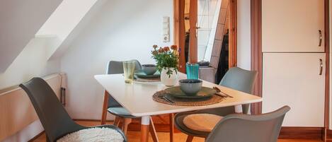 A dining area with a white table, grey chairs, a vase with flowers, and a blue glass.