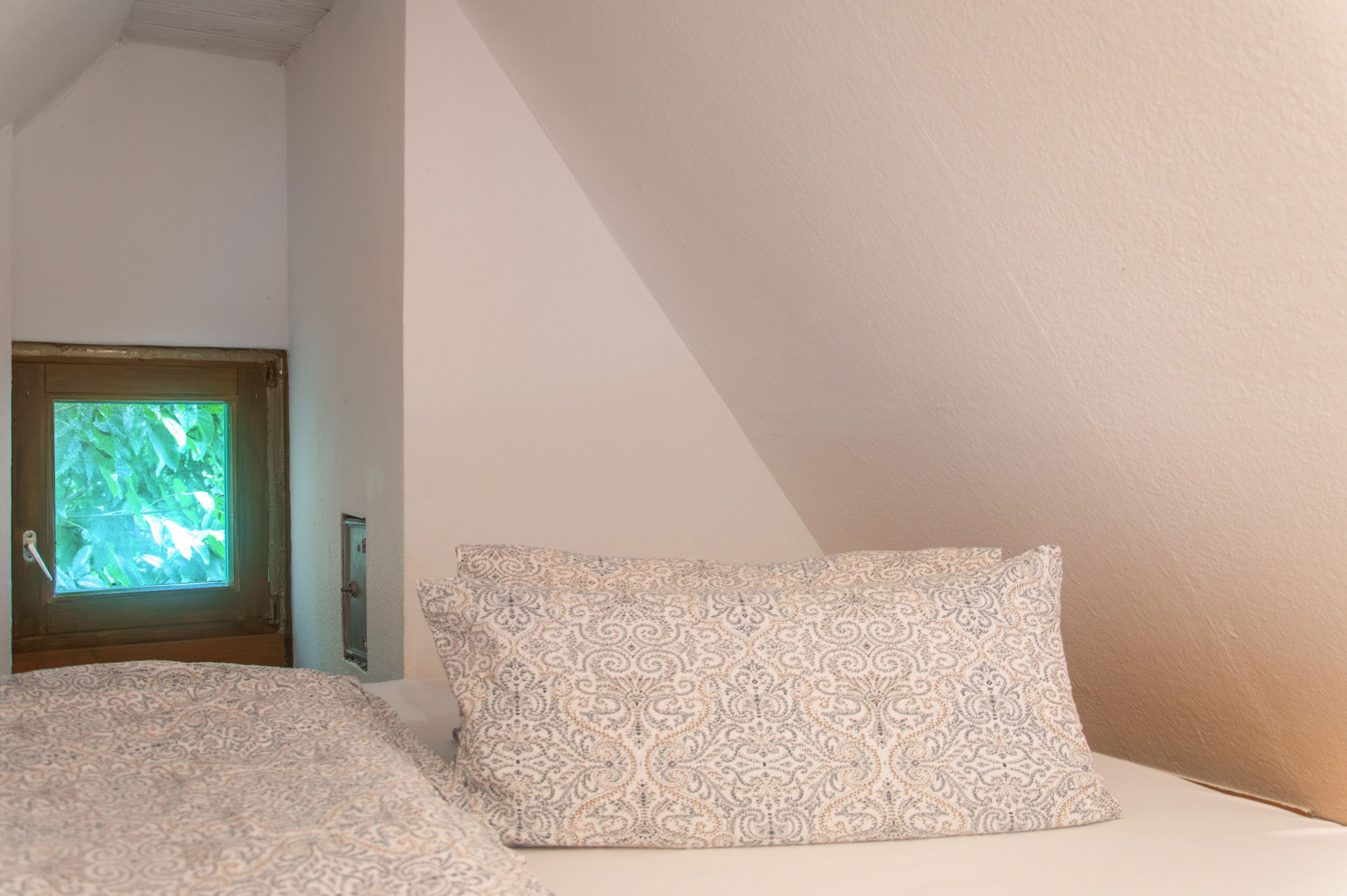 Una camera da letto con finestra, un letto con copriletto decorato e un punto luce a parete.