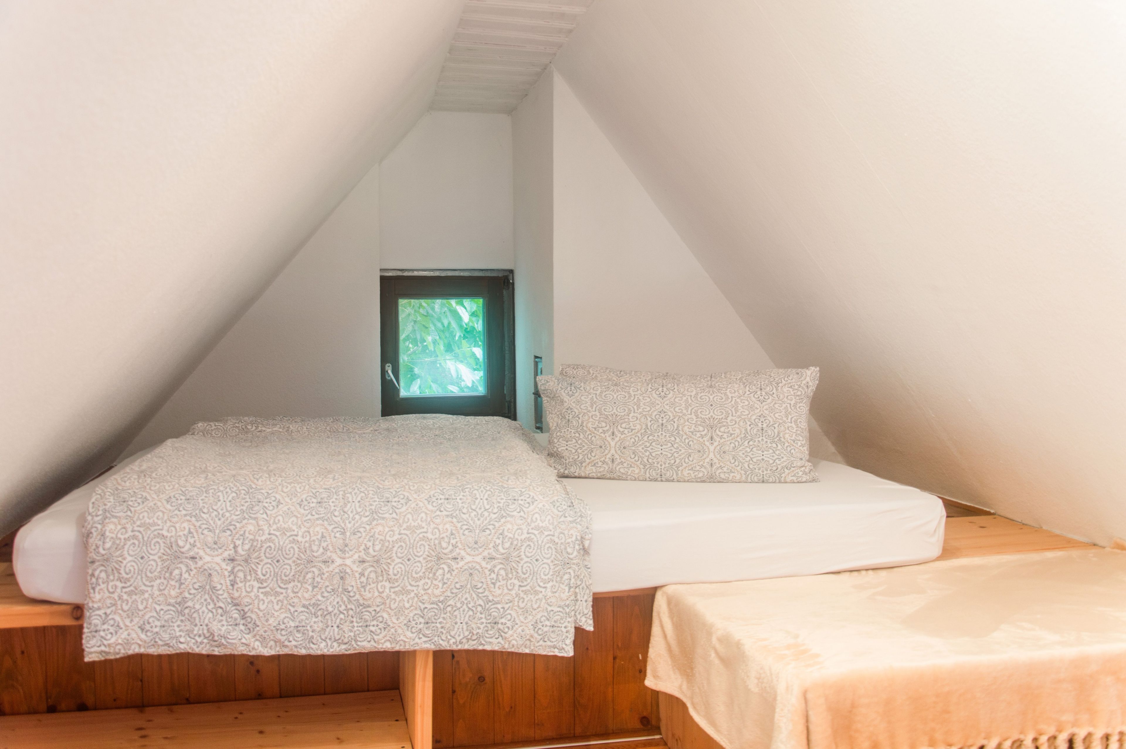 Ein kleiner, dreieckiger Raum mit einem Bett, einem Fenster und Holzdielen.