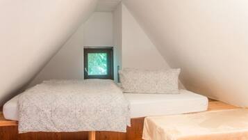 Ein kleiner, dreieckiger Raum mit einem Bett, einem Fenster und Holzdielen.