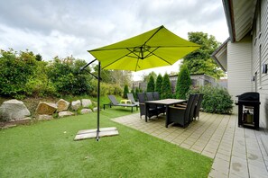 Eine Terrasse mit Tisch, Stühlen, einem gelben Sonnenschirm und einem Grill.