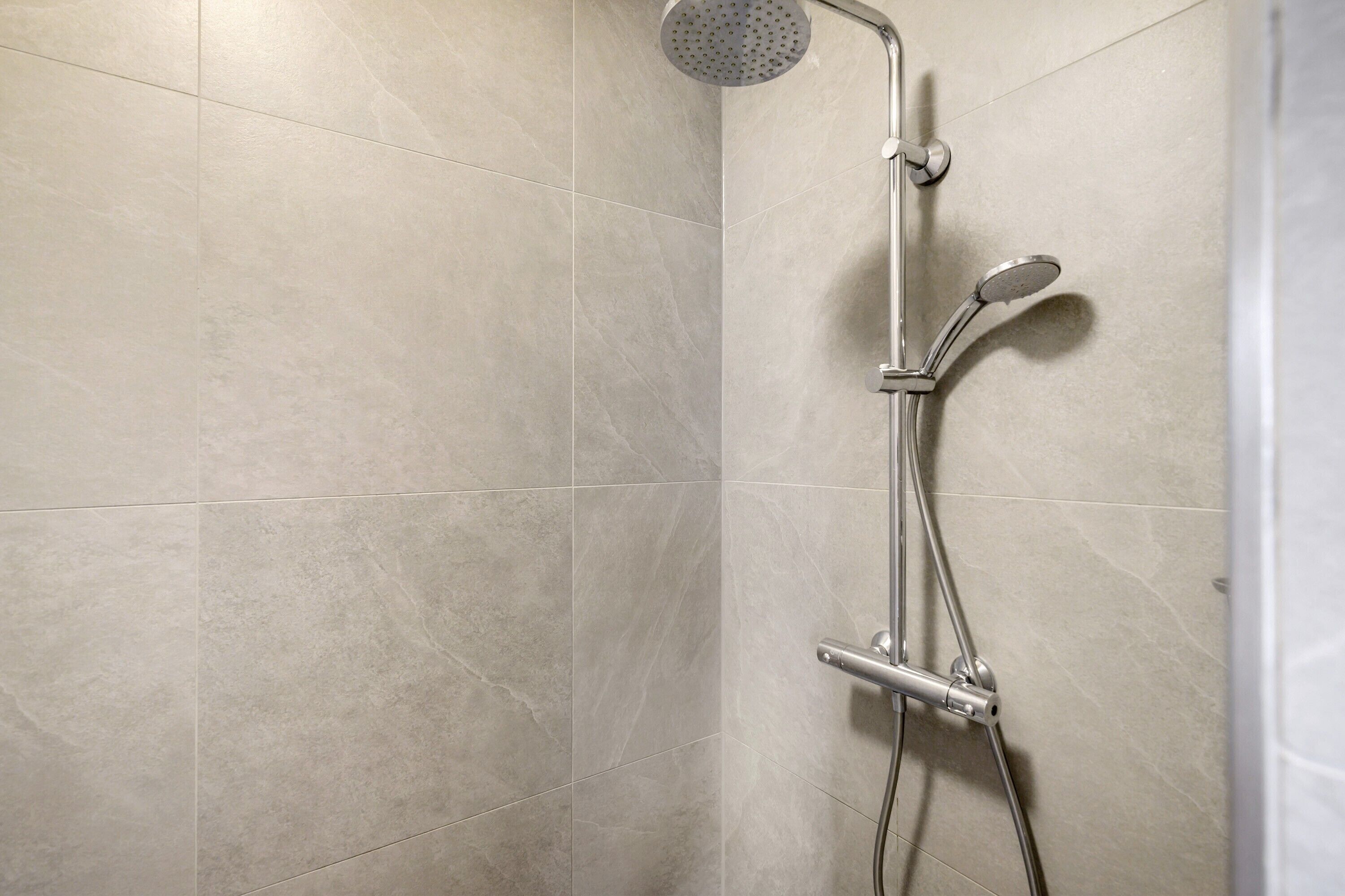 Une douche équipée d’un pommeau de douche à main et d’un robinet fixé au mur.