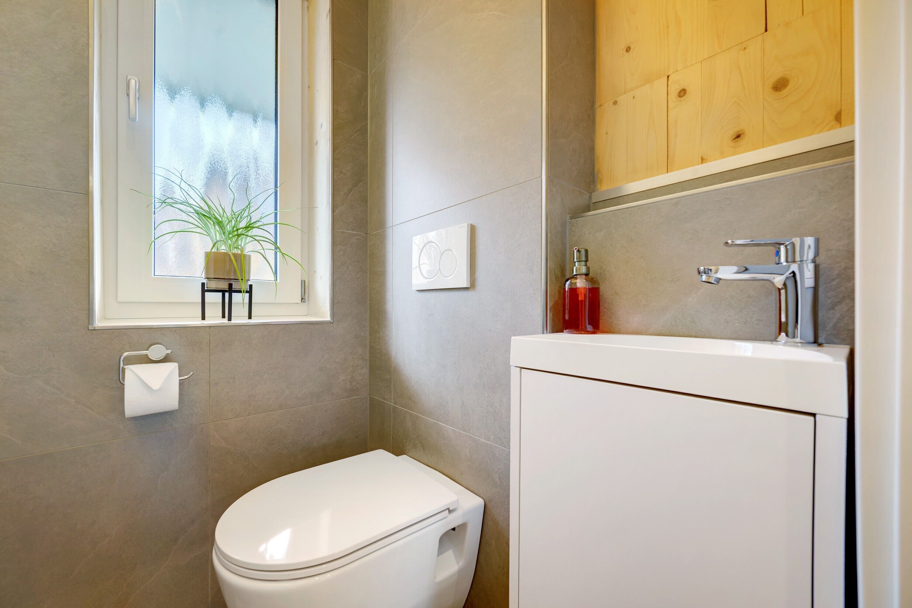 Ein Badezimmer mit Toilette, Waschbecken, einem Fenster mit Pflanze und einem Holzschrank.