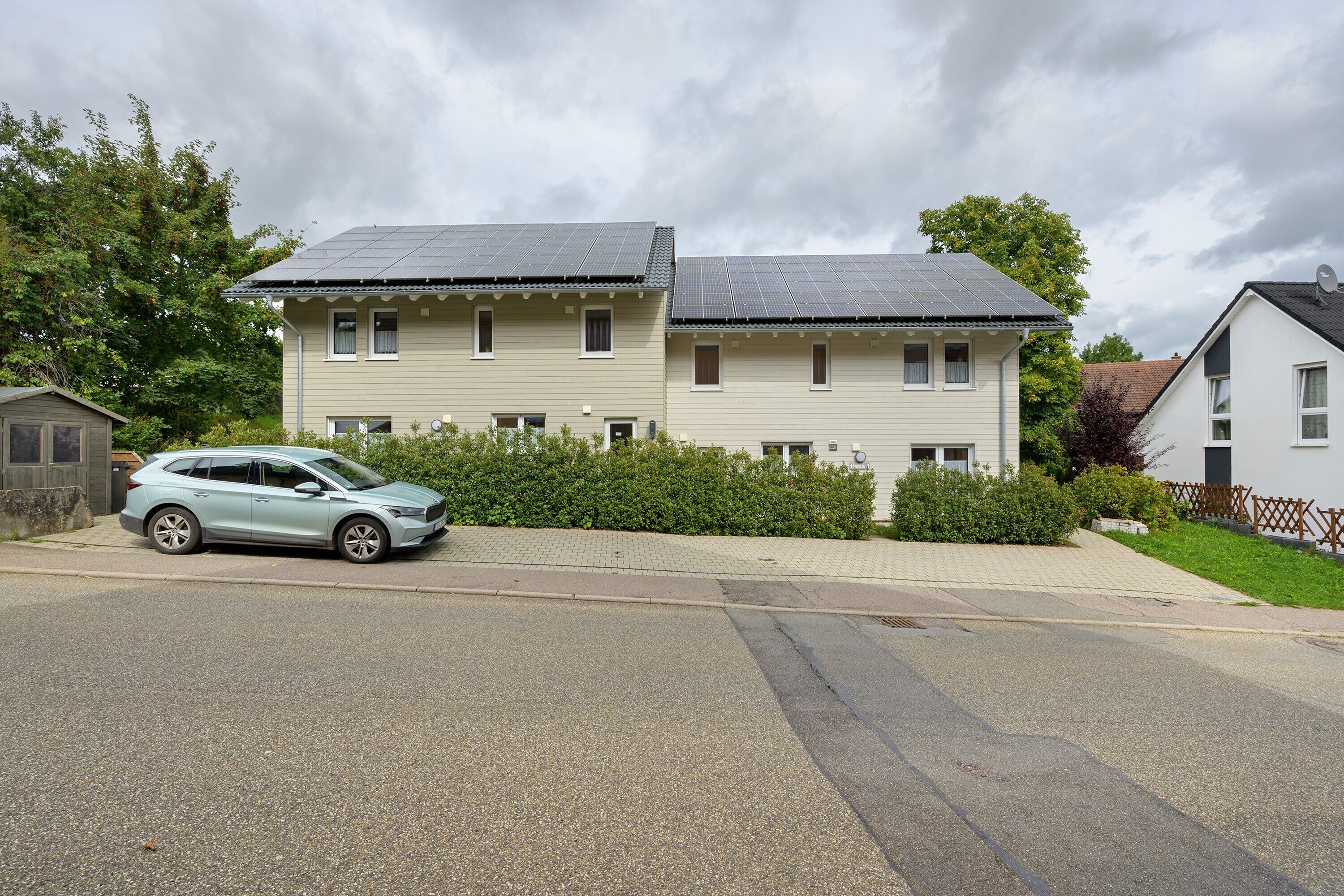 Ein zweistöckiges Haus mit Solaranlage auf dem Dach, einem geparkten Auto und einem gepflegten Rasen.