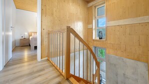 Een houten interieur met een trap, een bed, een nachtkastje en een raam.