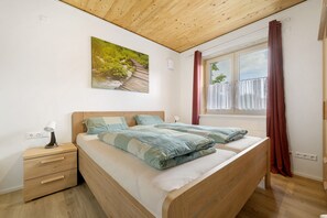 Une chambre à coucher avec un lit en bois, une table de chevet, une lampe, une fenêtre avec des rideaux et un tableau accroché au mur.