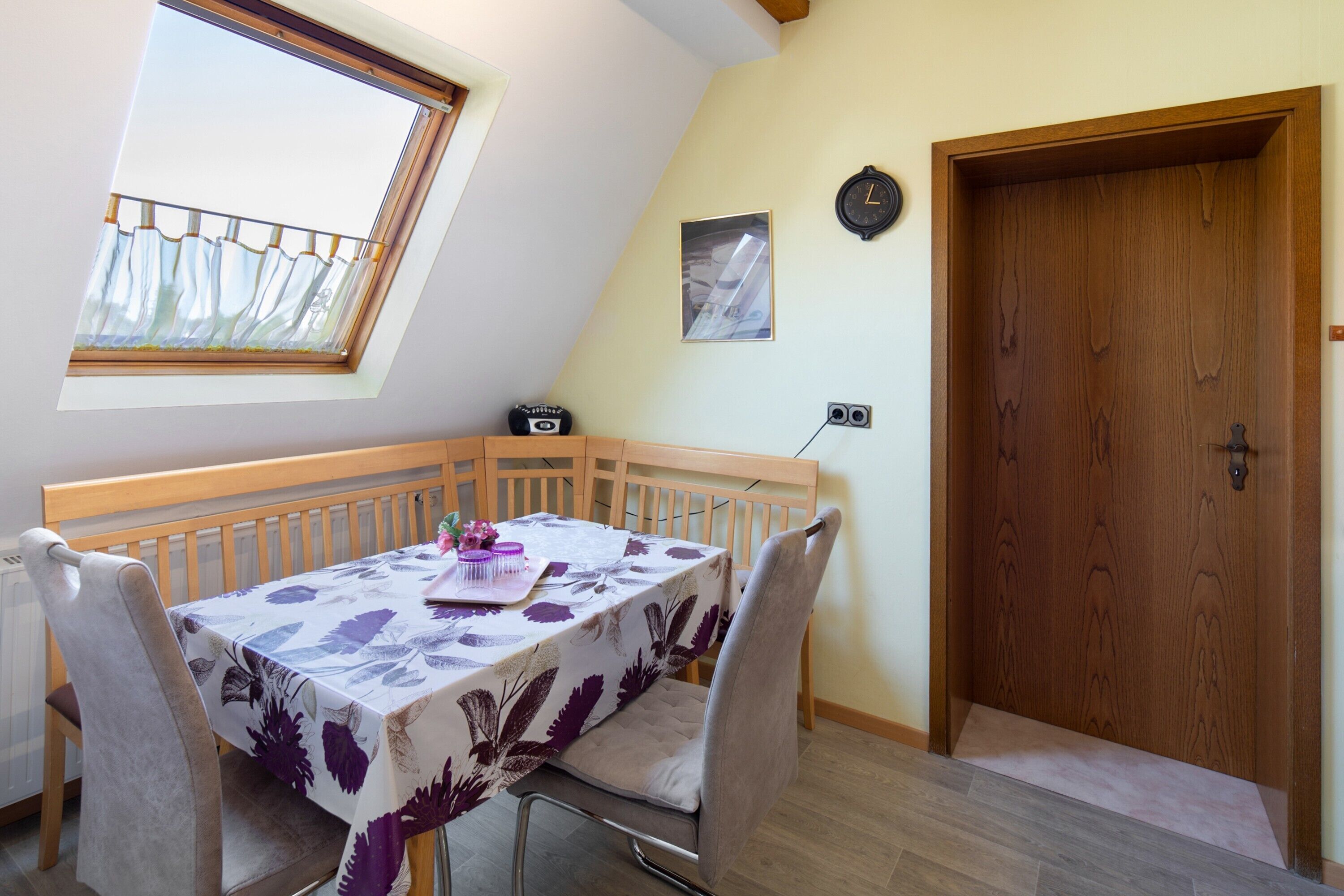 Een eetruimte met een tafel, stoelen, een klok en een houten deur.