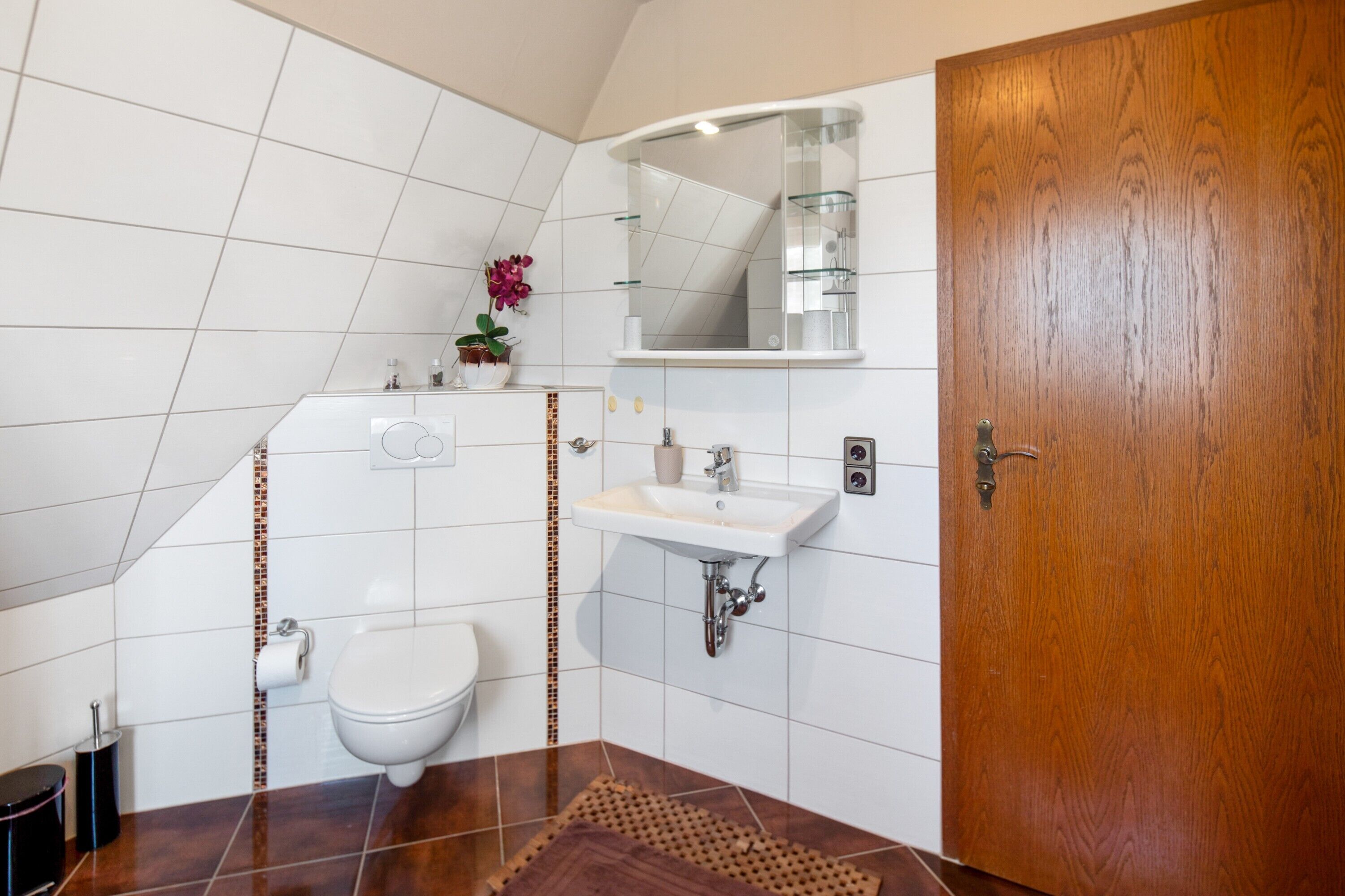 Un baño con inodoro, lavamanos, espejo y puerta de madera.
