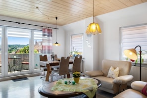 Un salon moderne avec un coin repas, de grandes fenêtres et une vue sur l’extérieur.