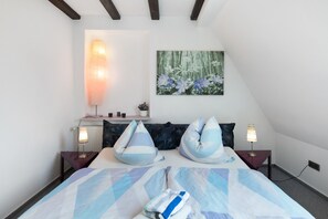 Une chambre à coucher comprenant un lit, deux tables de chevet, une lampe fixée au mur, un tableau et un radiateur.