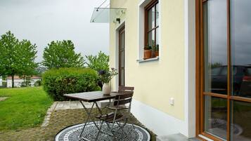 A patio with a table and chairs, a potted plant, and a window with a view of the surrounding greenery.