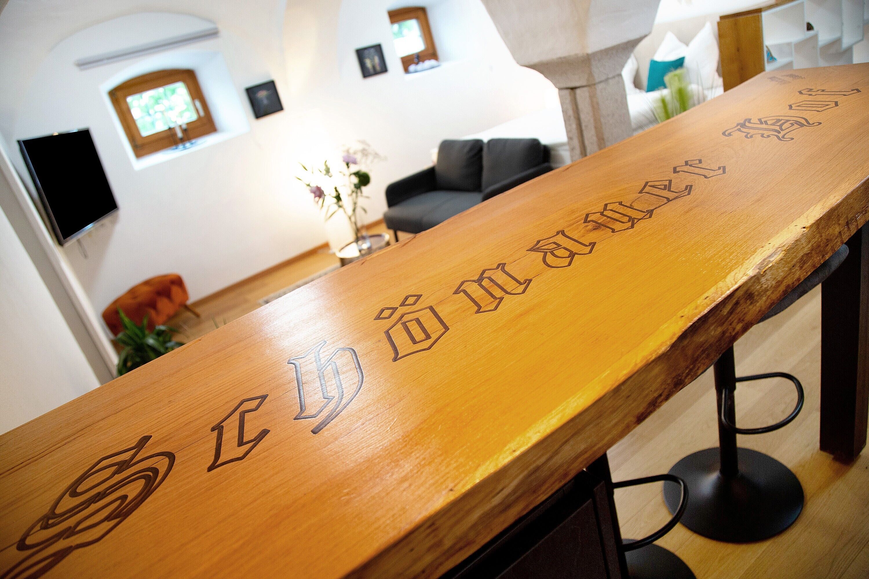 A wooden bar with carved text, a television mounted on the wall, and a sofa in the background.