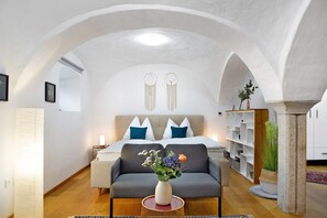 Un dormitorio con cama, sofá, mesita de noche, lámpara y un jarrón con flores.