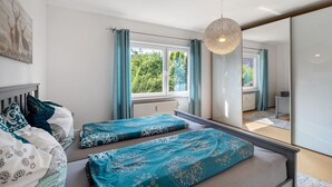 A bedroom with two beds, a large mirror, and a window with curtains.