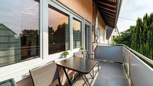 A balcony with a table and chairs, large windows, and a view of trees.