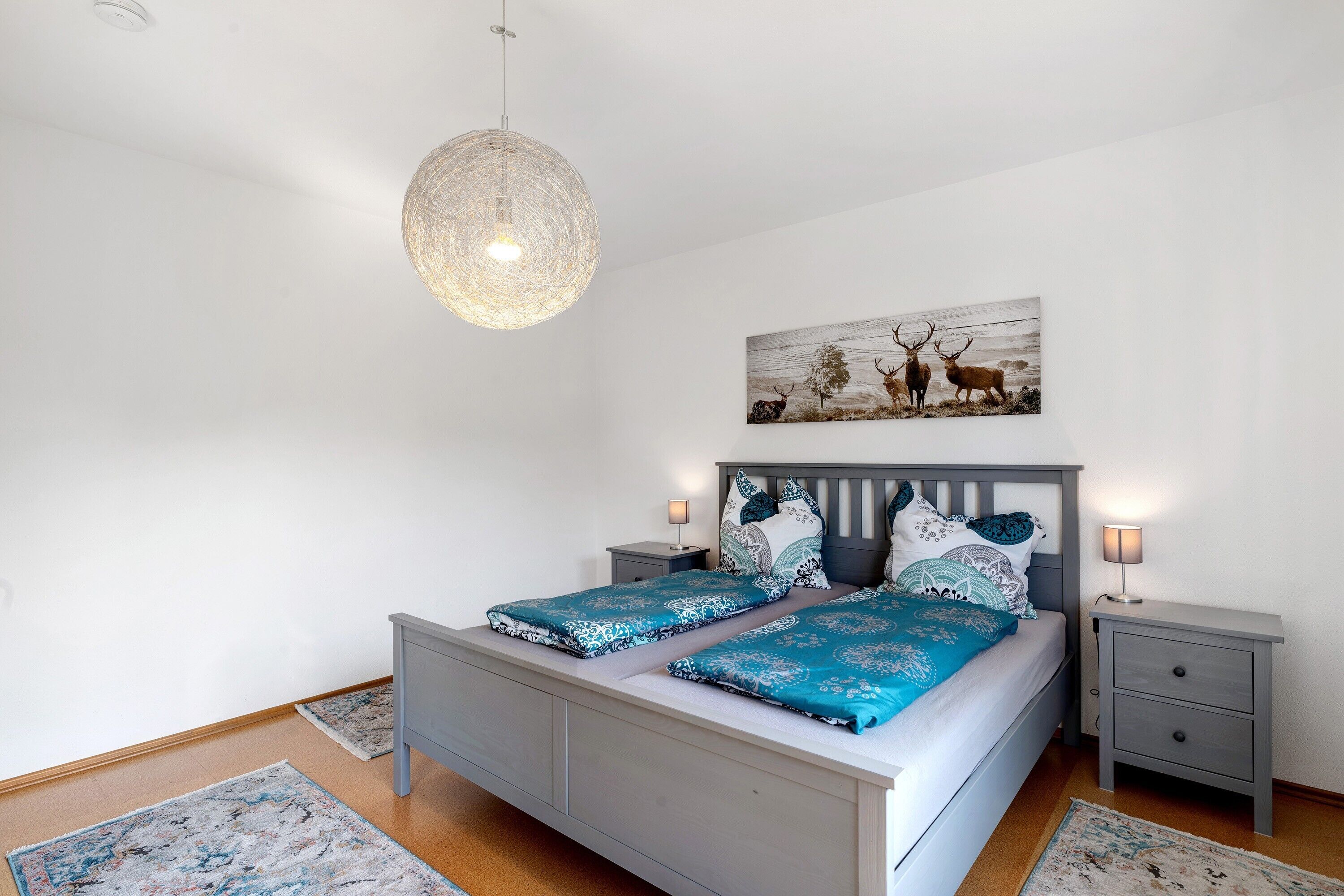 Un dormitorio con cama, mesitas de noche, lámpara colgante, un cuadro en la pared y una alfombra.