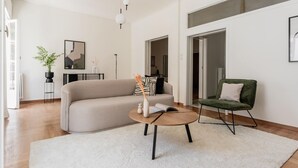 A modern living room with a sofa, a round coffee table, a green armchair, a potted plant, and a framed picture on the wall. - Acropolis Sunlight 2BR Aparment (Athina)