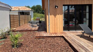 Een houten terras met buitenmeubilair, een barbecue en een zwembadgedeelte met ligbedden.