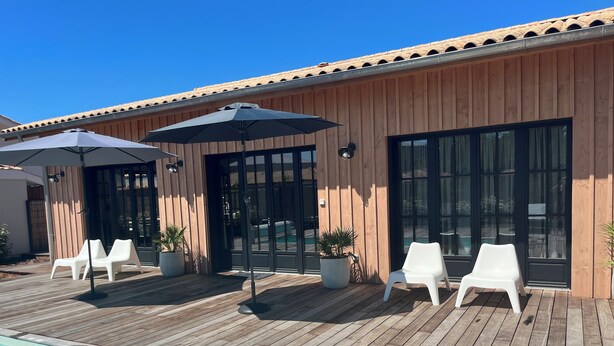 Een houten terras met een zwembad, witte ligbedden en parasols.