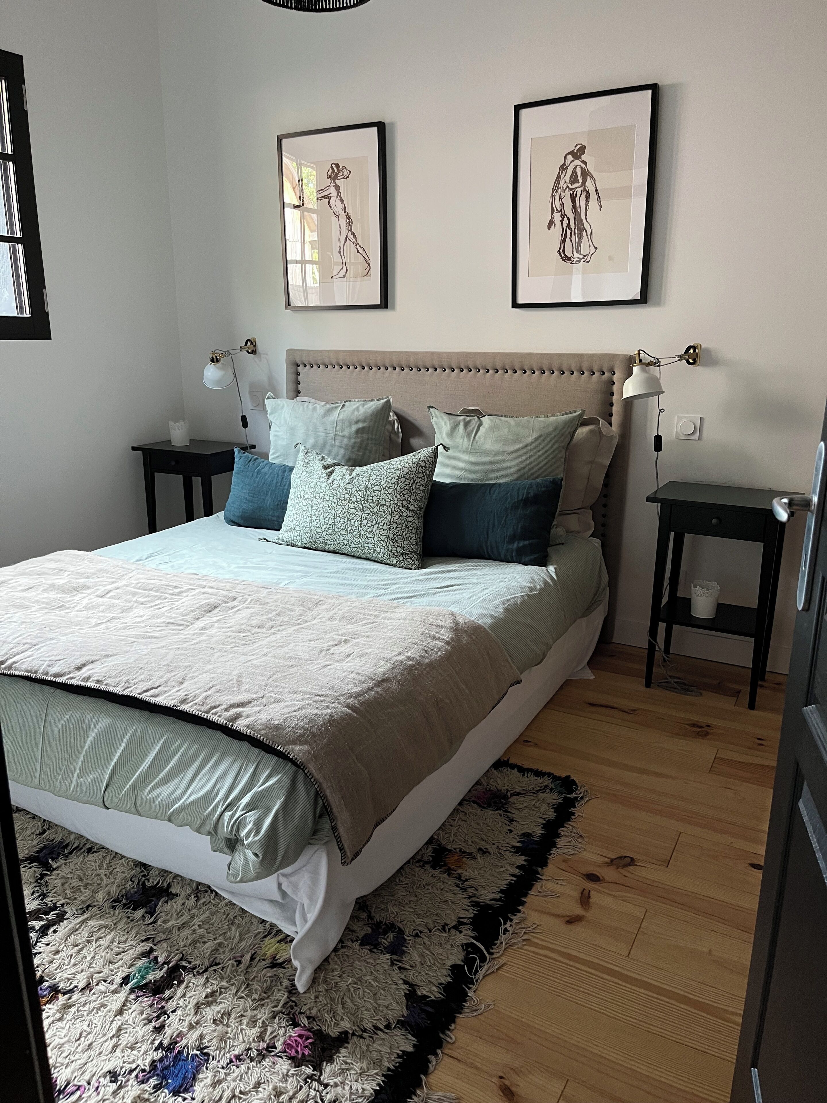 Une chambre à coucher comprenant un lit, des tables de chevet, un tapis et deux lampes fixées au mur.