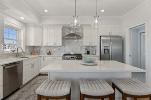 Une cuisine moderne avec des meubles blancs, un grand îlot central, des appareils en acier inoxydable et des luminaires suspendus.