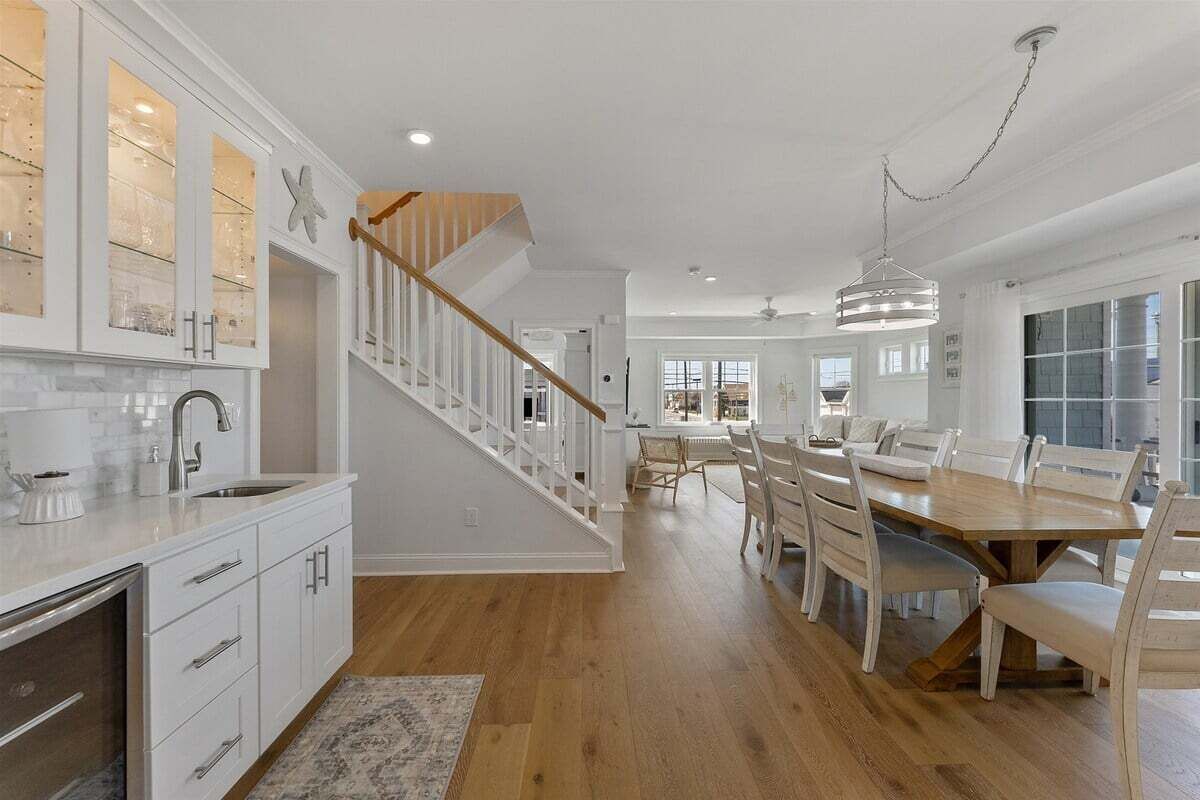 A spacious kitchen with white cabinetry, a wooden staircase, and a dining area with a large wooden table and chairs.