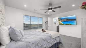 A bedroom with a bed, a ceiling fan, a large window, and a TV on the wall. - Luxury Townhome! Mountain Views! Family Amenities! Seasonal Pool & Pickleball! (American Fork)