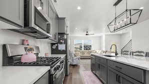 A modern kitchen with stainless steel appliances, a large island, and a view to a living area. - Luxury Townhome! Mountain Views! Family Amenities! Seasonal Pool & Pickleball! (American Fork)