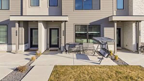 A modern townhouse with a covered patio, large windows, and a brick accent wall. - Luxury Townhome! Mountain Views! Family Amenities! Seasonal Pool & Pickleball! (American Fork)