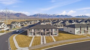 A suburban neighborhood with modern houses, a well-maintained street, and a mountain range in the background. - Luxury Townhome! Mountain Views! Family Amenities! Seasonal Pool & Pickleball! (American Fork)
