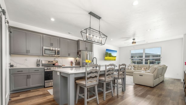 A modern kitchen with grey cabinets, a central island, and a dining area with four chairs. - Luxury Townhome! Mountain Views! Family Amenities! Seasonal Pool & Pickleball! (American Fork)