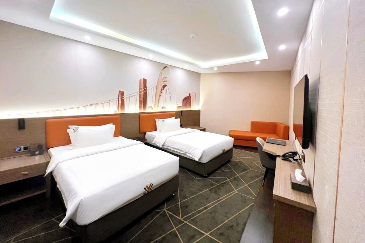 Une chambre d’hôtel avec deux lits, un bureau, une chaise, un téléviseur et un téléviseur fixé au mur.