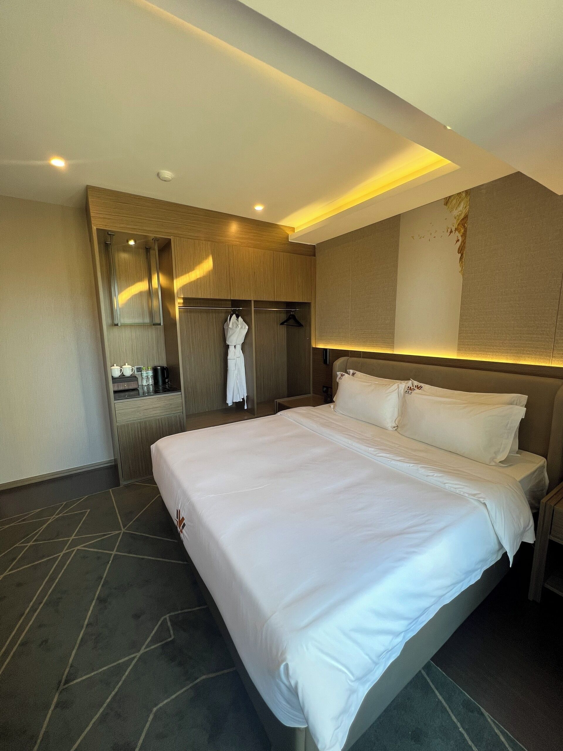 Una habitación de hotel con una cama grande, un vestidor amplio, una kitchenette pequeña y un baño.